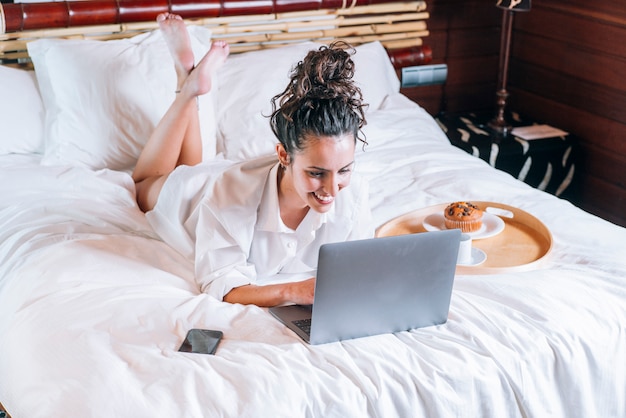 Pretty woman with phone and laptop in bed