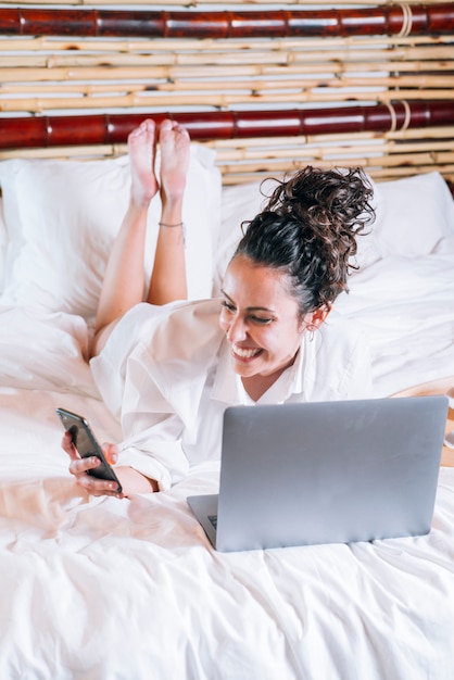 Pretty woman with phone and laptop in bed