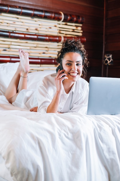 Pretty woman with phone and laptop in bed