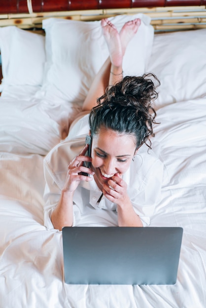 Pretty woman with phone and laptop in bed