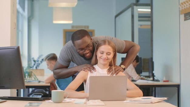 Photo pretty woman working on computer at coworking black man making massage