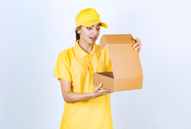 A pretty woman in yellow uniform holding an opened brown blank craft paper box .