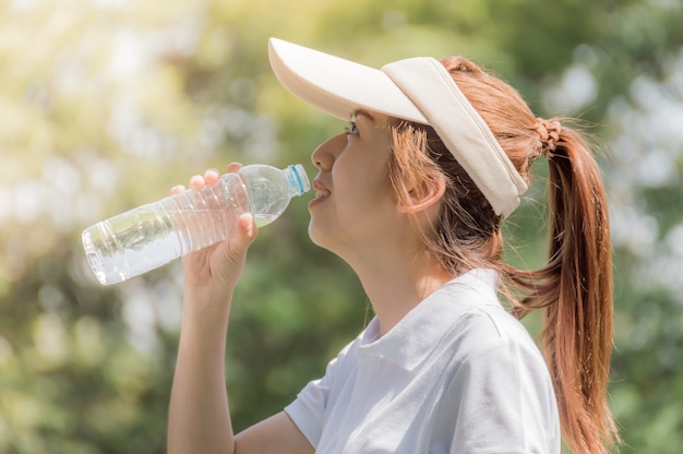 Atleti donne graziose bevono acqua dalle bottiglie di plastica