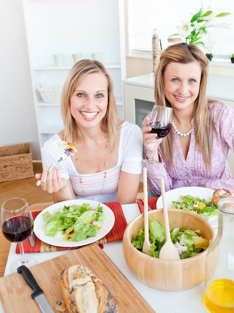 pretty women eating a salad and drinking wine in the kitchen
