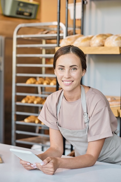 Pretty worker of bakery with tablet bending over workplace