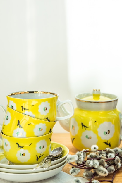 Photo pretty yellow tea set with stacked cups, saucers and pot, floral ornament, easter brunch