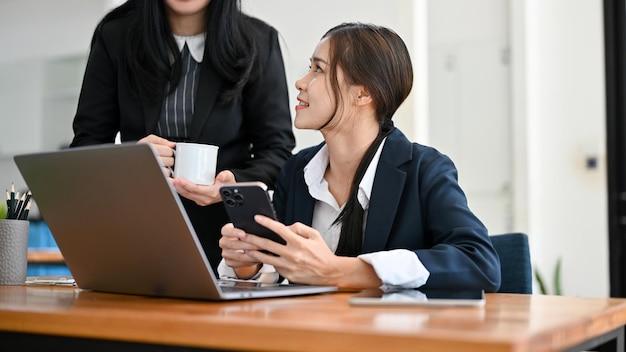 A pretty young Asian businesswoman talking with her female boss while working at her desk