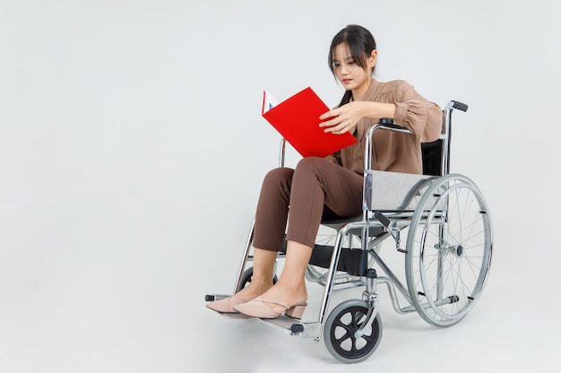 Pretty young asian girl as disability patient on hospital\
wheelchair study clinical report by reading physical health care\
and medical rehabilitation instruction for transporting injured or\
ill person