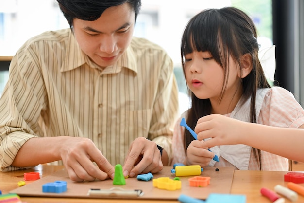 Pretty young asian girl enjoys playing play dough moulding\
colorful clay with her older brother