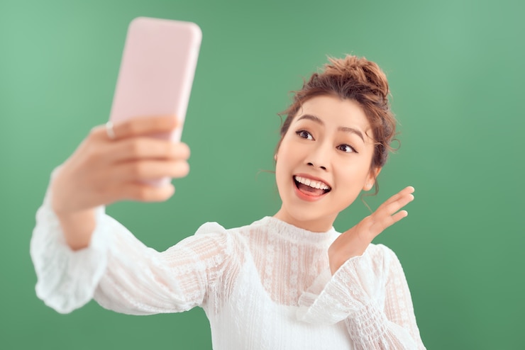 Photo 녹색 배경 위에 서 있는 동안 휴대 전화에 셀카 촬영을 하 고 꽤 젊은 아시아 여자.