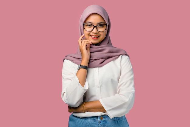 Pretty young asian woman smiling and wearing hijab on pink background