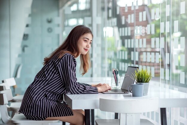 現代のオフィスでラップトップを持って机で働くかなり若いアジアの女性。