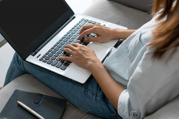 かなり若いアジアの女性が自宅の居間でノートパソコンを操作します。