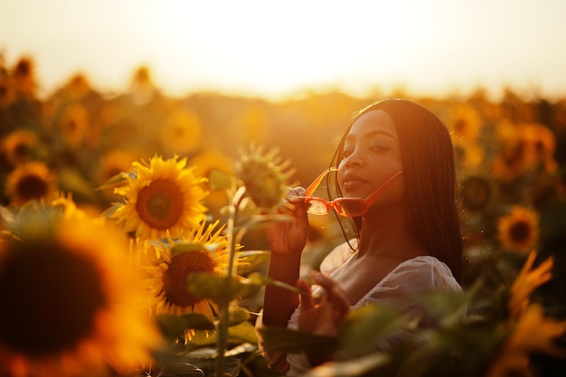 かなり若い黒人女性がひまわり畑で夏のドレスポーズを着ています。