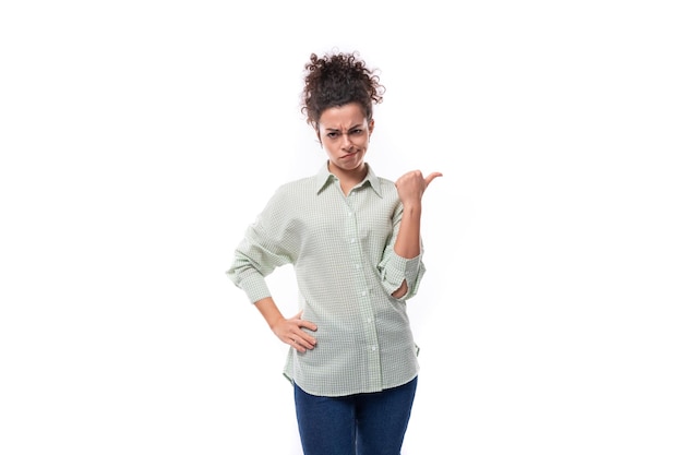 Foto una giovane bella donna riccia dai capelli neri con un panino di stile disattento in una camicia punta con disprezzo