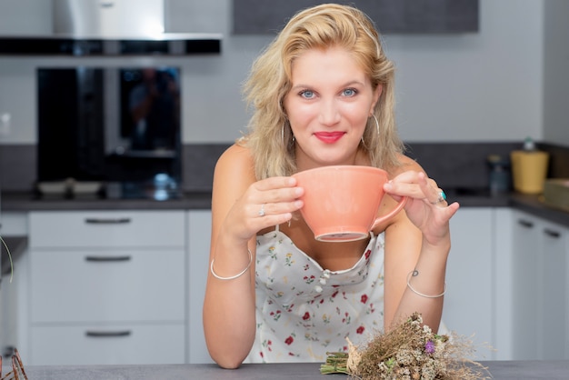 Pretty young blond woman drinking coffee in the kitchen