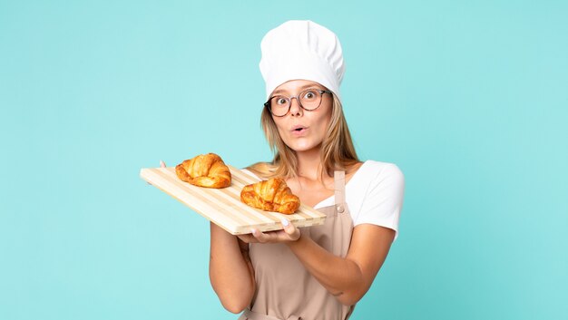 Donna chef bionda abbastanza giovane che tiene un vassoio di croissant