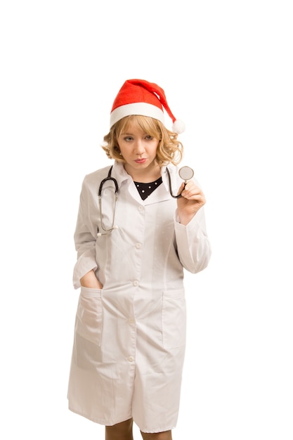 Довольно молодая блондинка врач или медсестра в шляпе Санта-Клауса и лабораторном халате празднуют Рождество в больнице