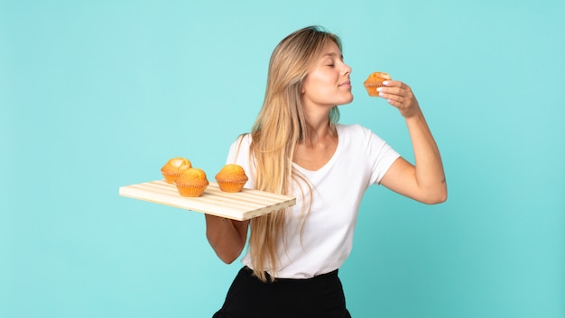 Pretty young blonde woman holding a muffins tray