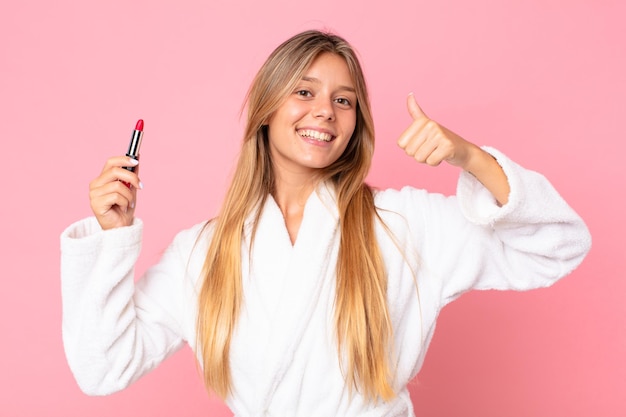 バスローブを着て、口紅を持っているかなり若いブロンドの女性