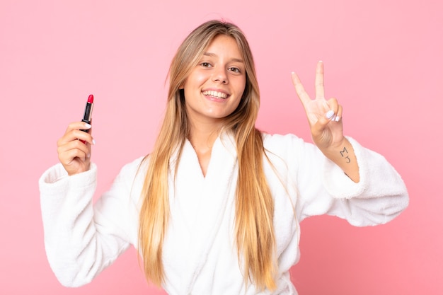 Pretty young blonde woman wearing bath robe and holding a lipstick