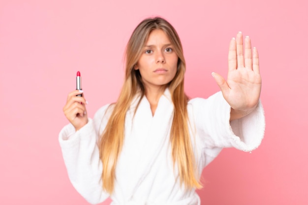 Pretty young blonde woman wearing bath robe and holding a lipstick