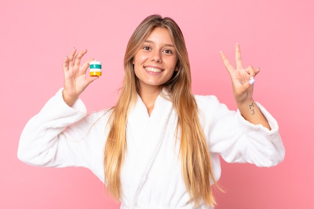 Photo pretty young blonde woman wearing bathrobe and holding a cosmetic product