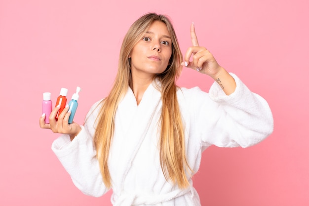 pretty young blonde woman wearing bathrobe and holding a cosmetic product
