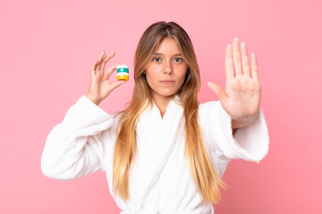 Pretty young blonde woman wearing bathrobe and holding a cosmetic product