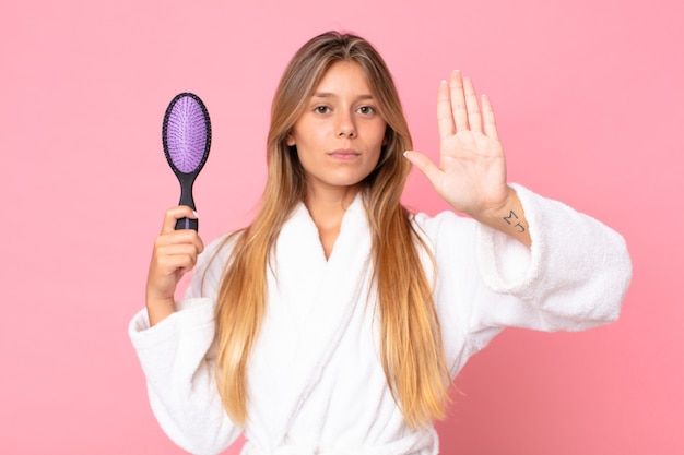 バスローブを着て、ヘアブラシを持っているかなり若いブロンドの女性