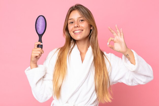 バスローブを着て、ヘアブラシを持っているかなり若いブロンドの女性