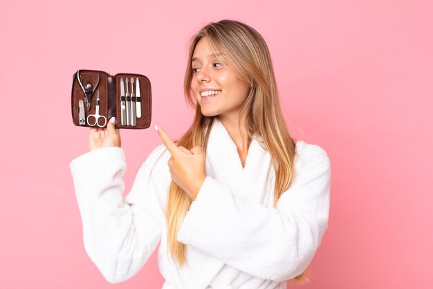 Pretty young blonde woman wearing bathrobe and holding a make up bag with nails tools