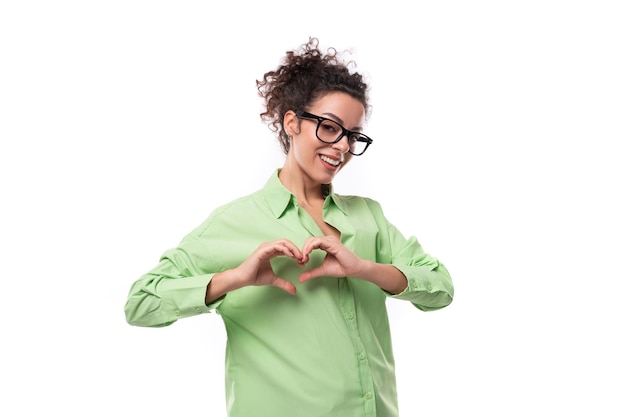 Foto una bella giovane bruna ricciola donna con gli occhiali è vestita con una camicia verde su uno sfondo bianco con