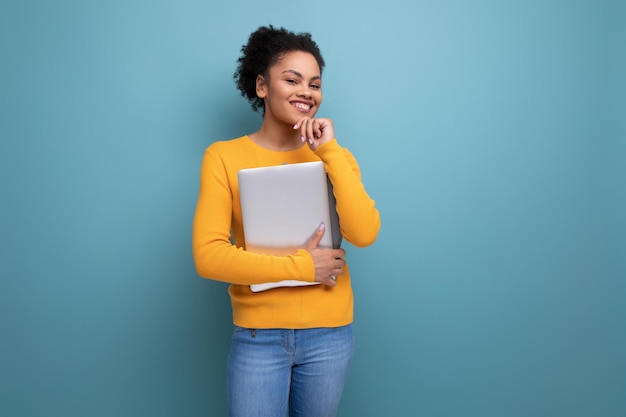 Pretty young brunette latin female adult in yellow sweater holding a laptop in her hands