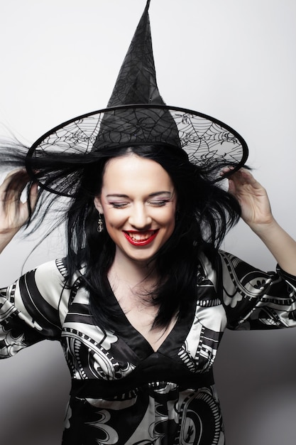 Pretty young brunette witch with black hat, isolated against white background