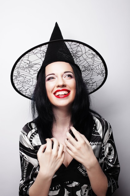 Pretty young brunette witch with black hat, isolated against white background