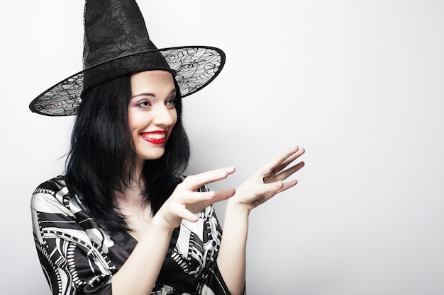 Pretty young brunette witch with black hat, isolated against white background