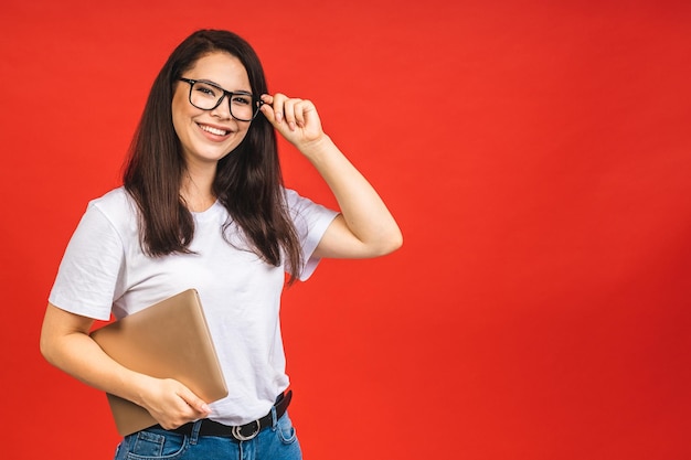 Pretty young business woman in casual holding laptop in the office isolated over red background Working with computer