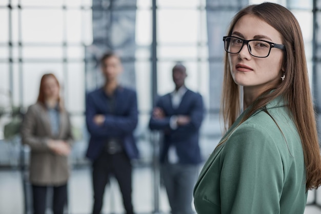 Pretty young business woman in an elegant green jacket standing in the office and looking at the cam