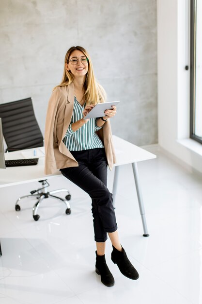 Pretty young business woman holding digital tablet and standing in the modern office