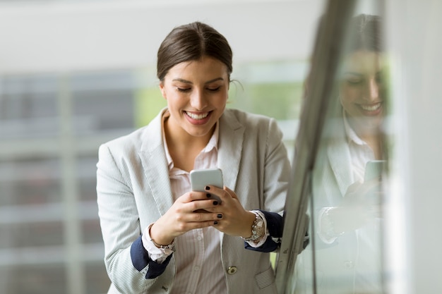 Pretty young business woman stands on the stairs at the office and use mobile phone