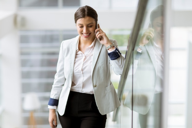 Pretty young business woman stands on the stairs at the office and use mobile phone