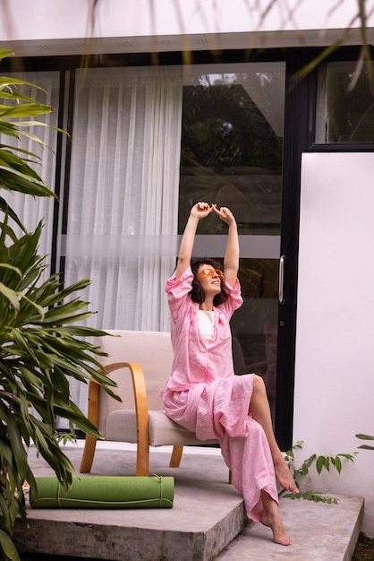 Pretty young caucasian brunette woman stretches her arms up sitting on chair outdoors Concept of rest and recovery