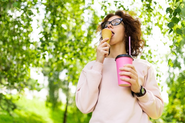 かなり若い白人女性はコーヒーとアイスクリームのある公園で散歩に行く