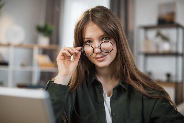 Pretty young caucasian woman with long dark hair sitting at table with modern laptop