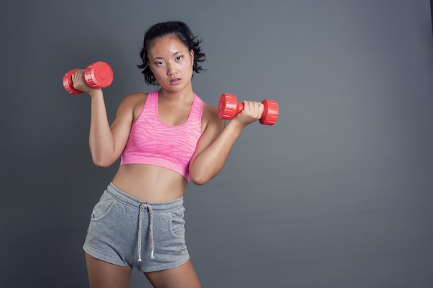 Pretty young chinese girl exercising with dumbbells looking straight ahead