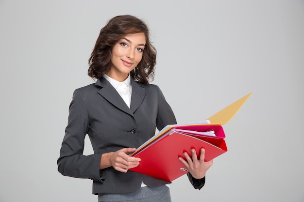 Pretty young curly happy smiling business woman in gray suit working with colorful folders