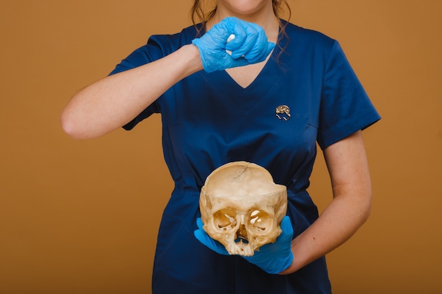 A pretty young doctor pours vitamin capsules into a human skull. The doctor pours pills on the background.