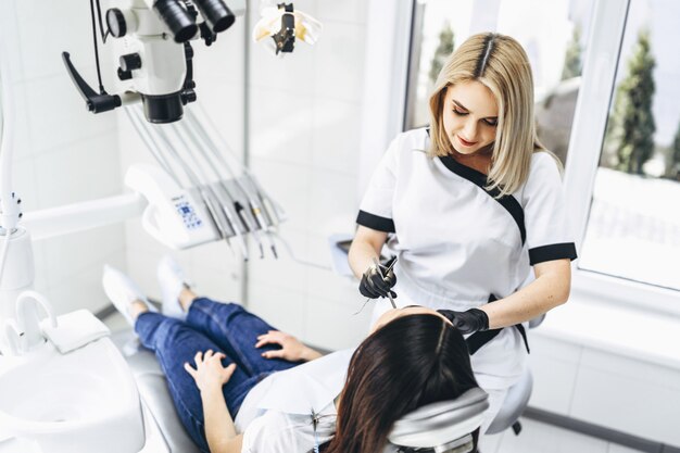 Pretty young female dentist making examination and treatment for young female patient in dental clinic.