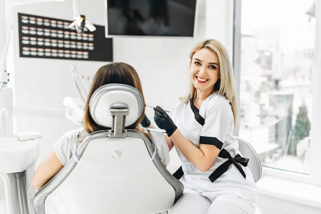 Pretty young female dentist making examination and treatment for young female patient in dental clinic.